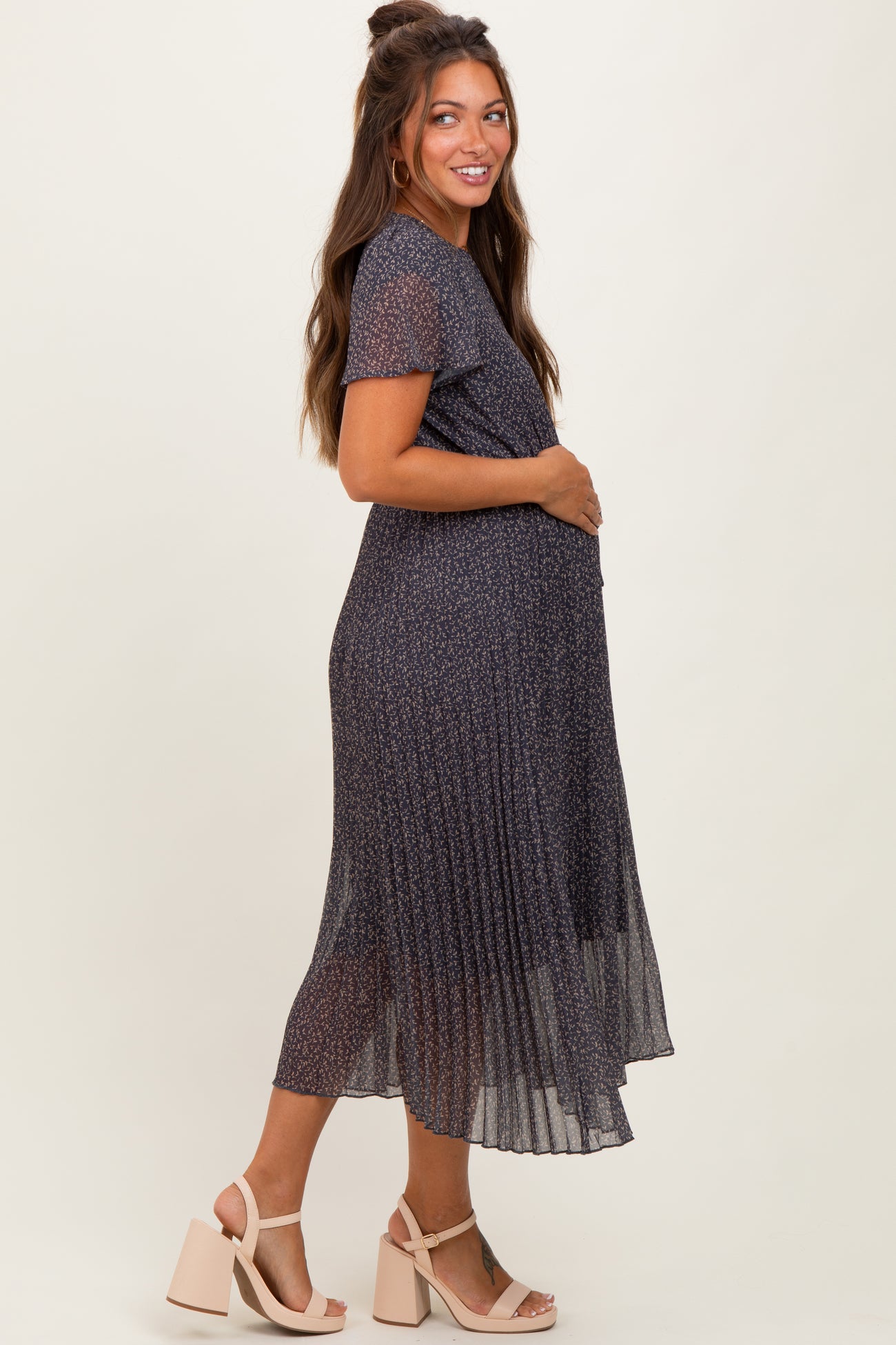 woman wearing a navy floral midi maternity dress with short sleeves and a pleated skirt, showcasing her baby bump