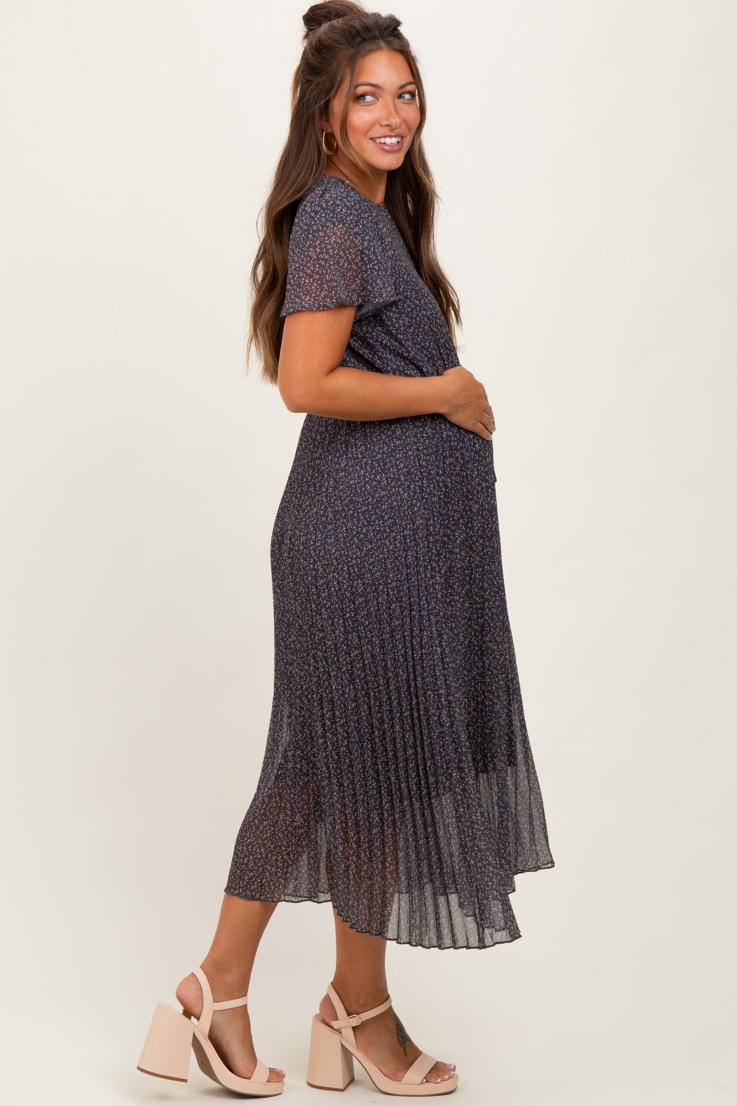 woman wearing a navy floral midi maternity dress with short sleeves and a pleated skirt, showcasing her baby bump