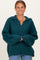 woman wearing a teal oversized knitted sweater with a v-neck and a collar, smiling and posing with hands clasped
