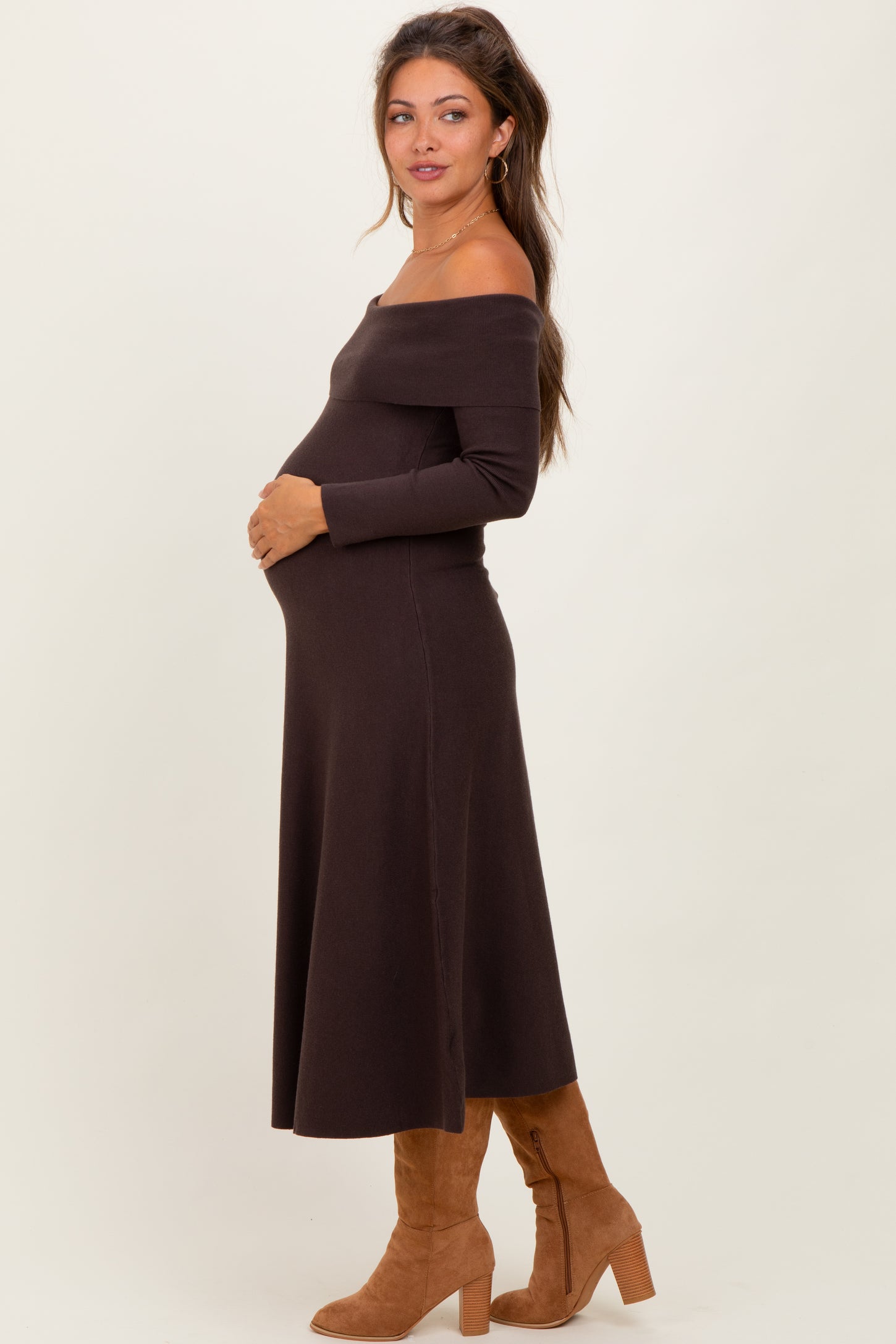 woman wearing a dark brown off-shoulder maternity dress and holding her baby bump