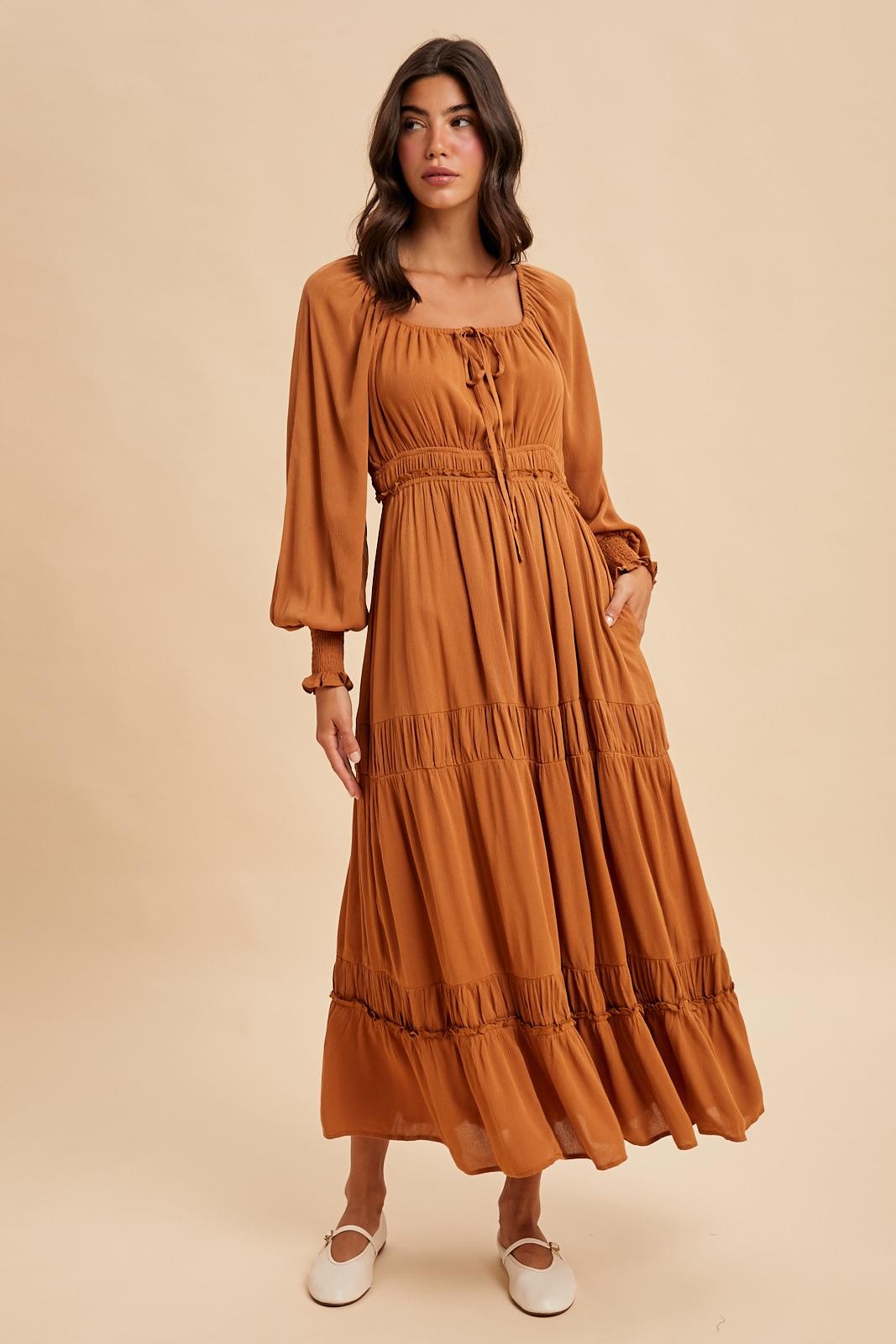 woman wearing a rust-colored long sleeve maxi dress with a cinched waist and ruffled tiers