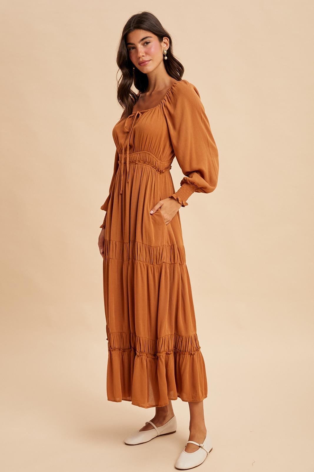 woman wearing a rust-colored maxi dress with puff sleeves and ruffle details, standing against a neutral background