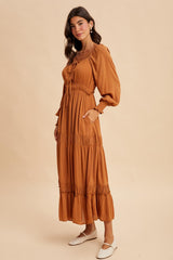 woman wearing a rust-colored maxi dress with puff sleeves and ruffle details, standing against a neutral background