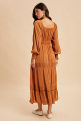 woman wearing a rust-colored long sleeve maxi dress with tiered ruffles and a smocked waist, seen from the back