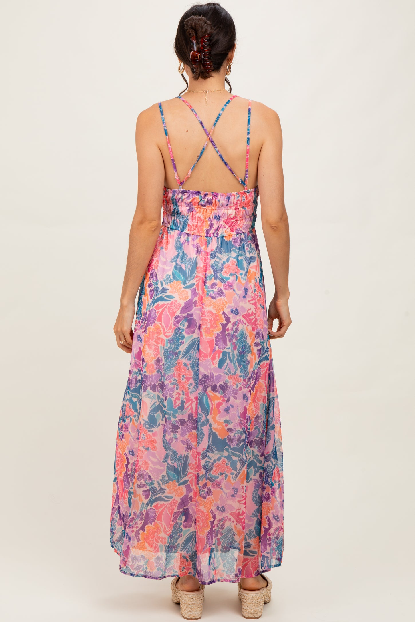 woman wearing a colorful floral maxi dress with crisscross straps and a smocked waist, seen from the back