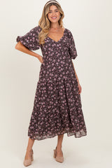 woman wearing a floral printed black maternity dress with a v-neck and puff sleeves, smiling and posing with one hand on her hip