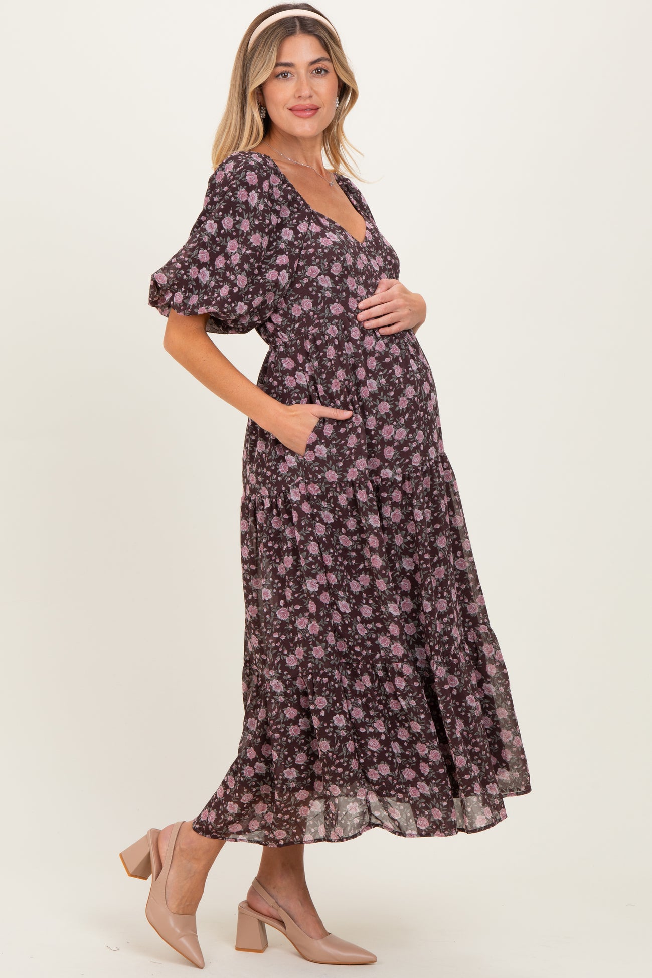 woman wearing a black floral print maternity dress with puff sleeves and pockets, showcasing her baby bump