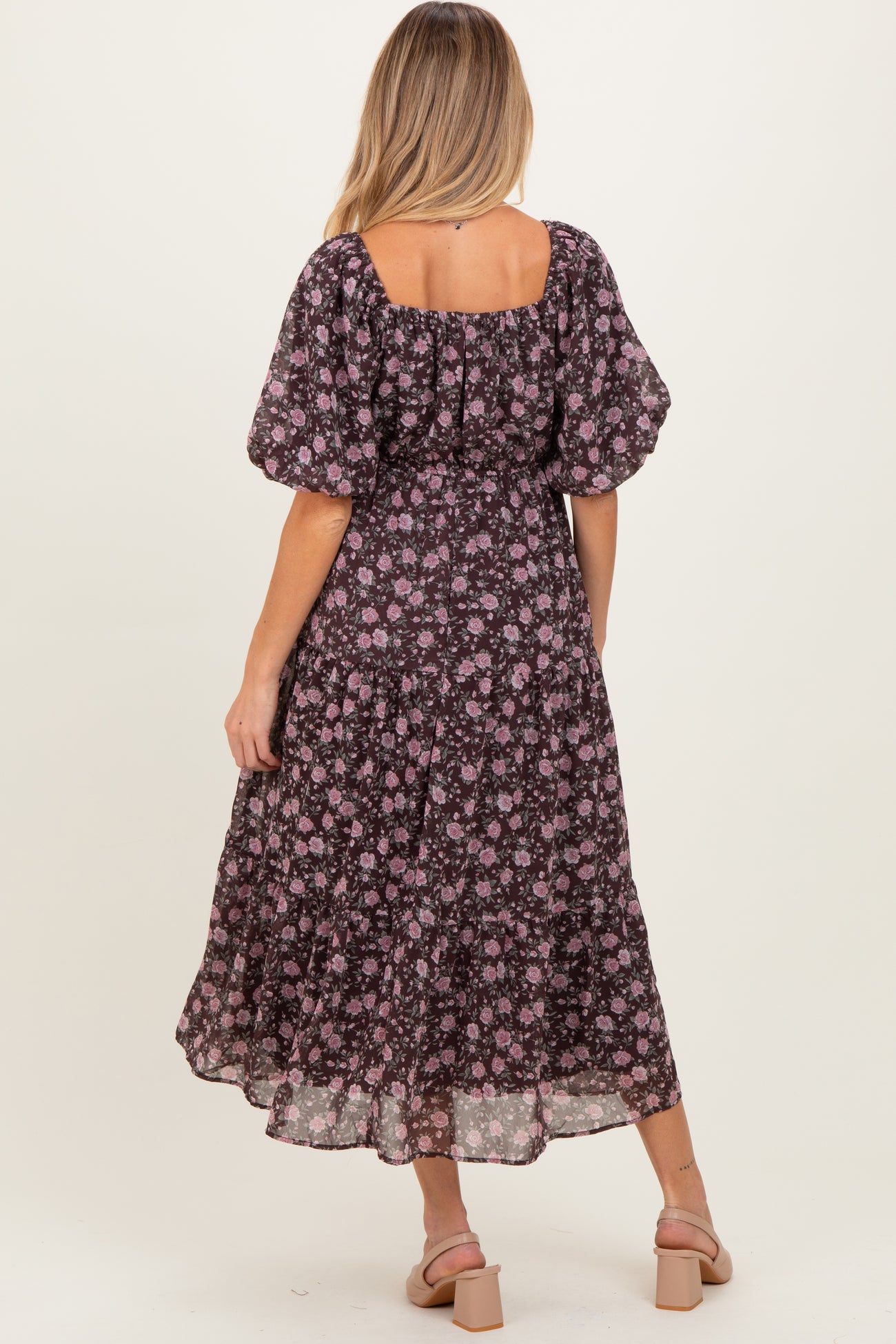 woman wearing a black floral maternity dress with puff sleeves and a tiered skirt, showing a baby bump.