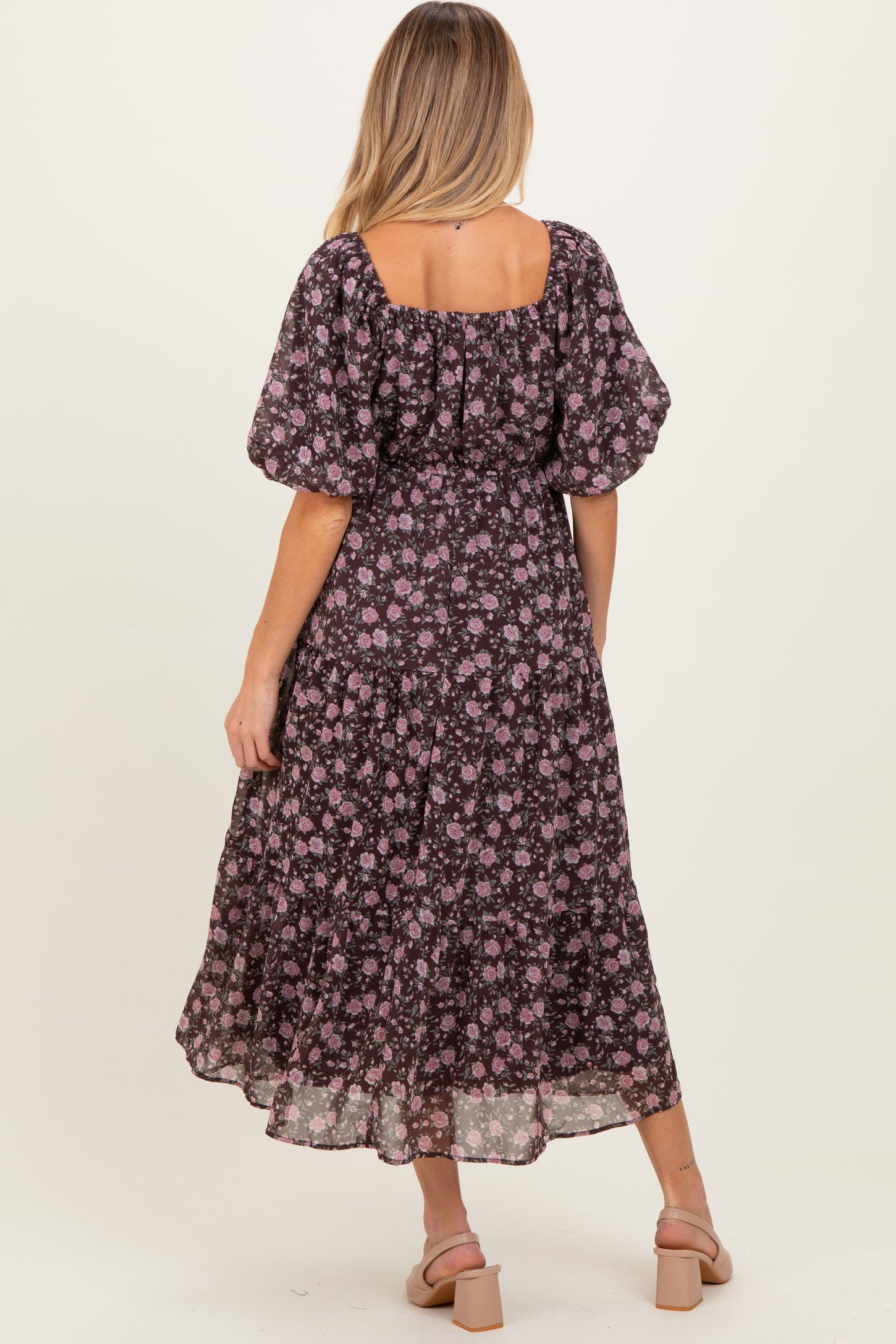 woman wearing a black floral maternity dress with puff sleeves and a tiered skirt, showing a baby bump.