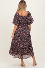 woman wearing a black floral maternity dress with puff sleeves and a tiered skirt, showing a baby bump.