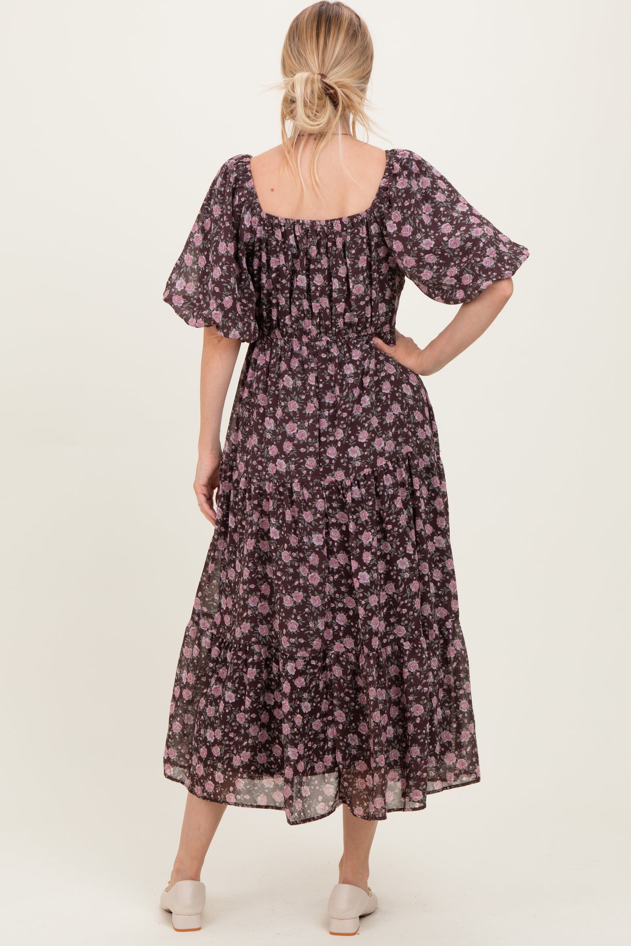 woman wearing a black floral maxi dress with short flutter sleeves and a tiered skirt, viewed from the back