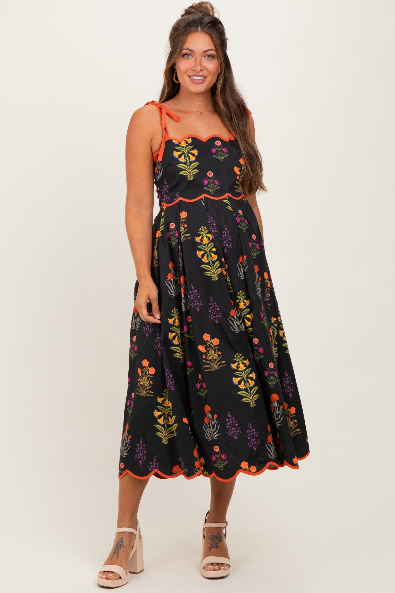 woman wearing a black floral maternity dress with orange accents and spaghetti straps, highlighting her baby bump