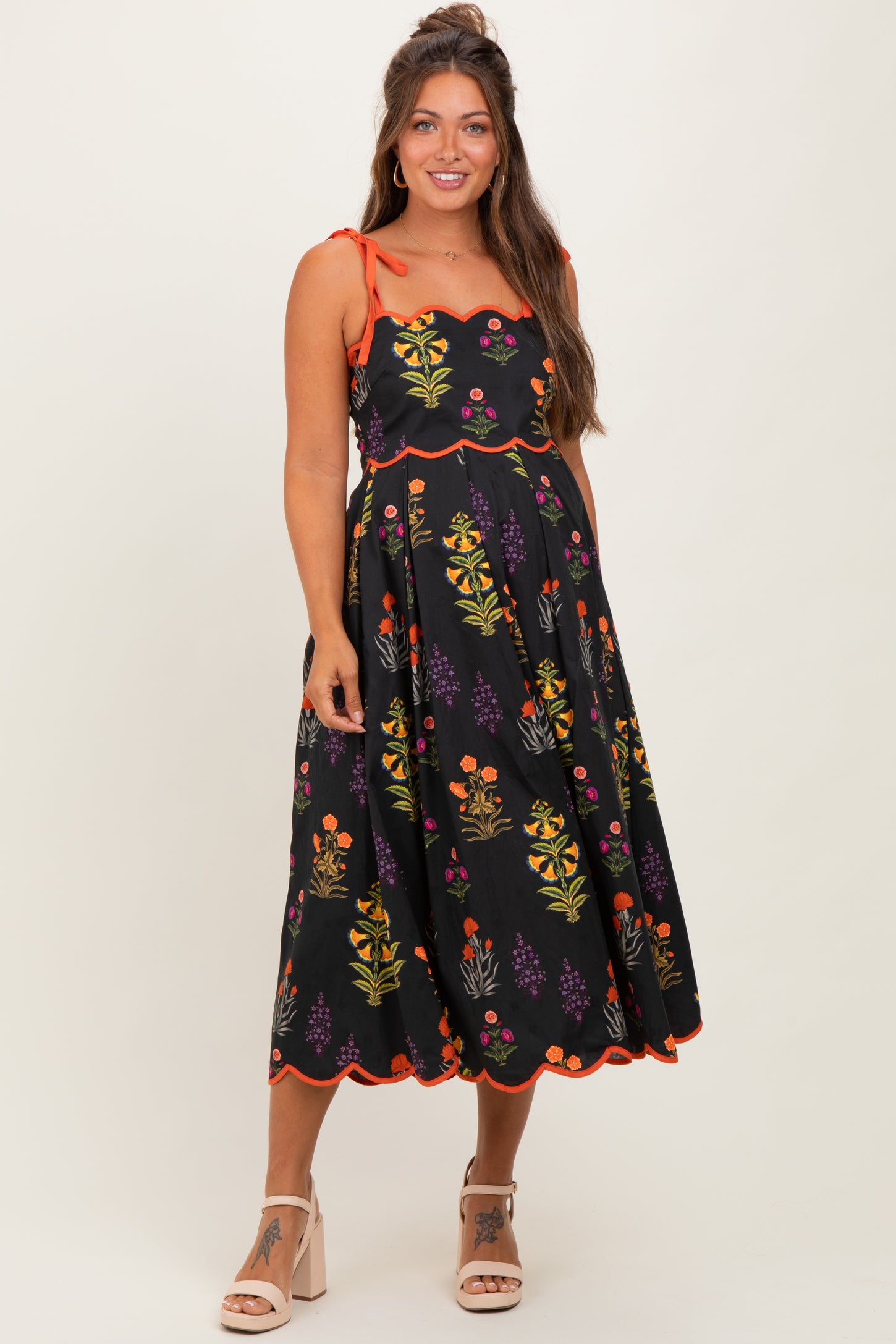 woman wearing a black floral maternity dress with orange accents and spaghetti straps, highlighting her baby bump