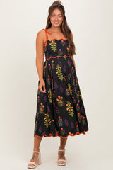 woman wearing a black floral maternity dress with orange accents and spaghetti straps, highlighting her baby bump
