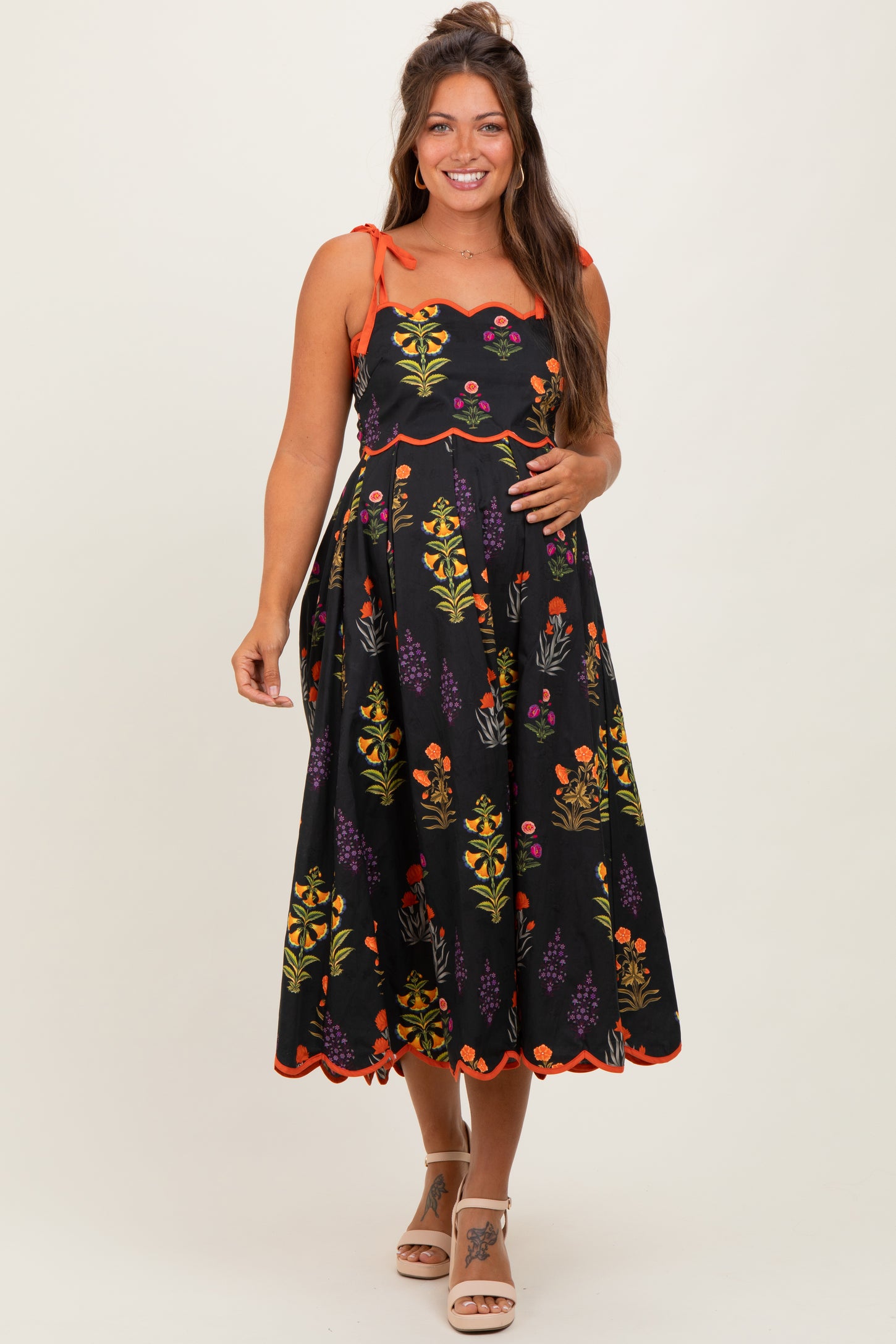 woman wearing a black floral maternity dress with adjustable straps and scalloped hem, showcasing her baby bump
