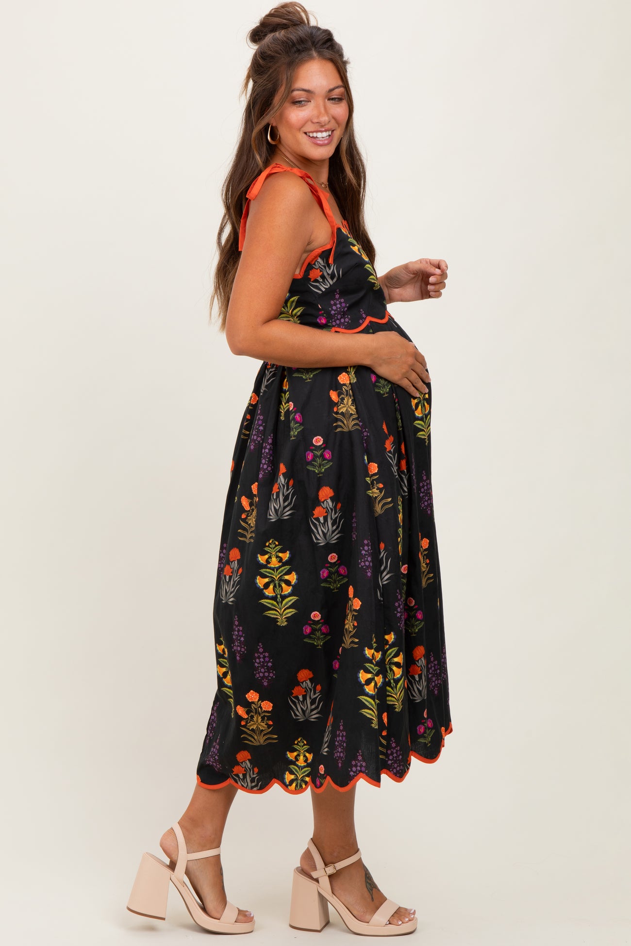 woman wearing a black maternity dress with colorful floral patterns and ruffled straps, showing her baby bump