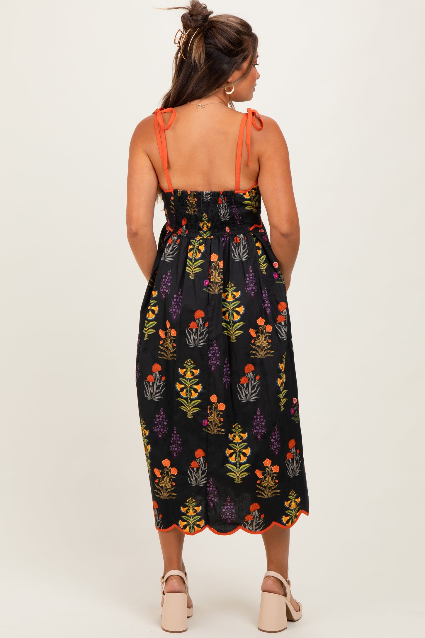 woman wearing a black floral maternity sundress with orange straps and a smocked back, showing her baby bump
