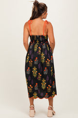 woman wearing a black floral maternity sundress with orange straps and a smocked back, showing her baby bump