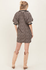 woman wearing a short leopard print dress with puff sleeves and black and white striped details, standing with her back to the camera