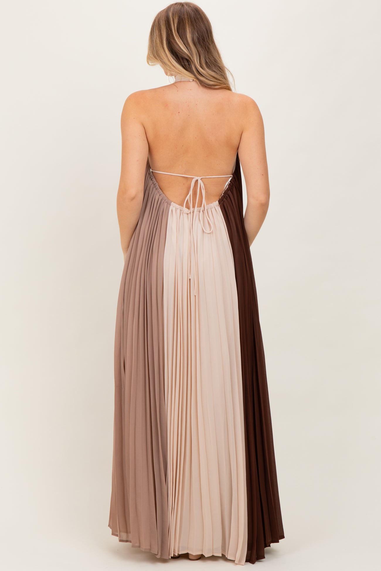 woman wearing a backless color-blocked maxi dress with pleated fabric in shades of beige and brown
