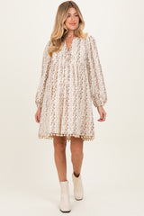 woman wearing a beige floral maternity dress with long sleeves and pom-pom trim, showcasing her baby bump