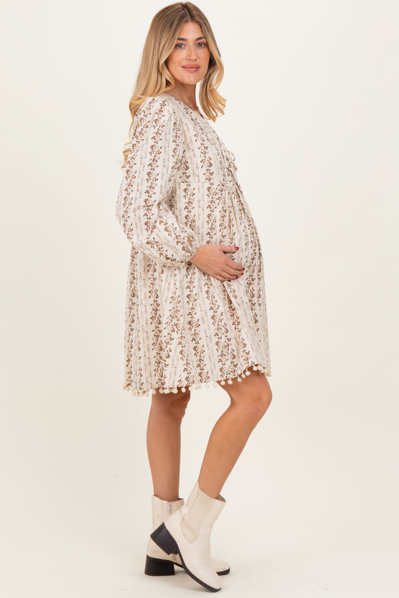 woman wearing a cream maternity dress with floral print and long sleeves, holding her baby bump