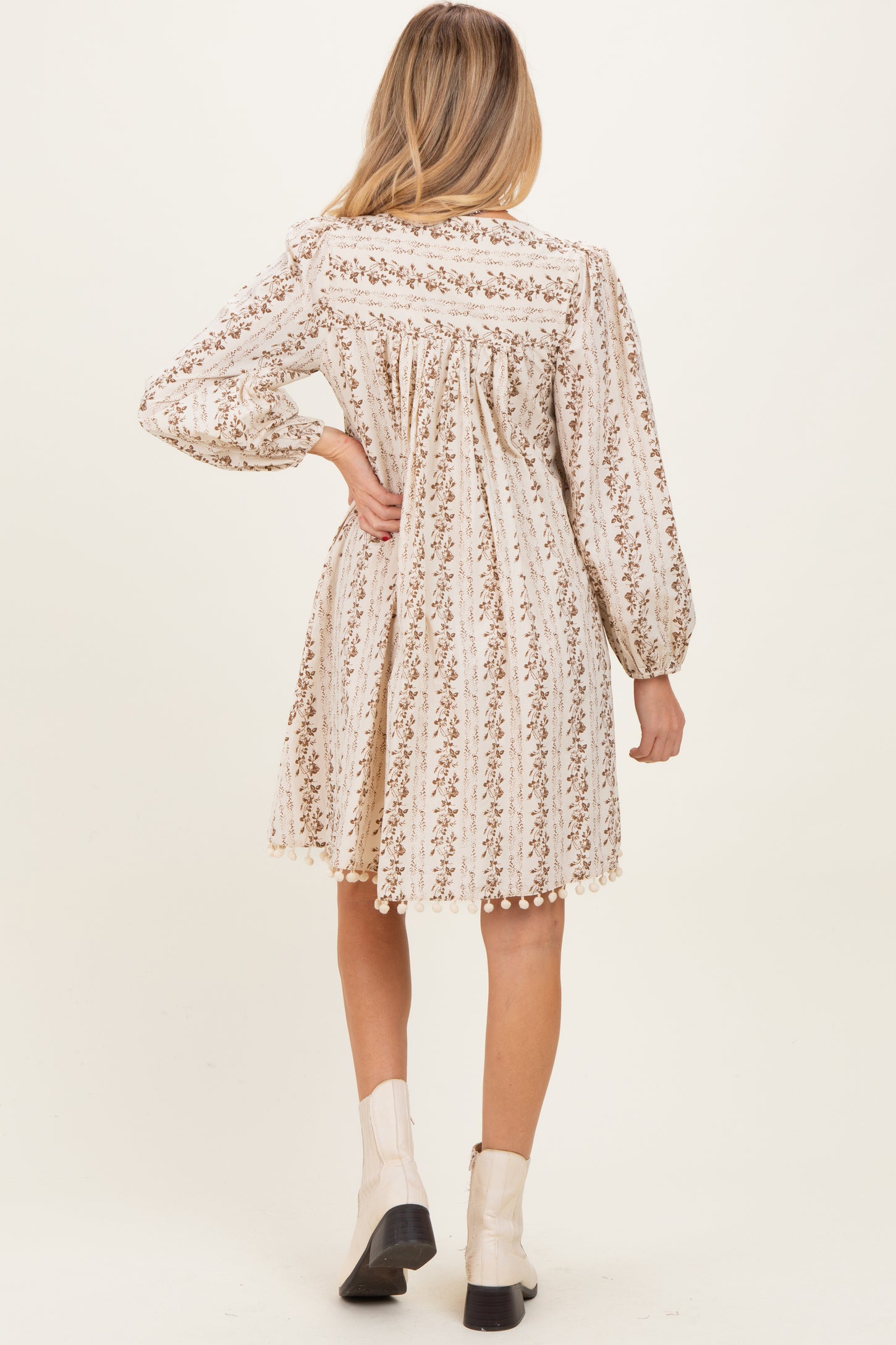 woman wearing a cream floral print long sleeve maternity dress with gathered back and pom-pom details