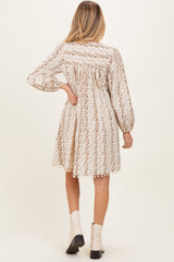 woman wearing a cream floral print long sleeve maternity dress with gathered back and pom-pom details
