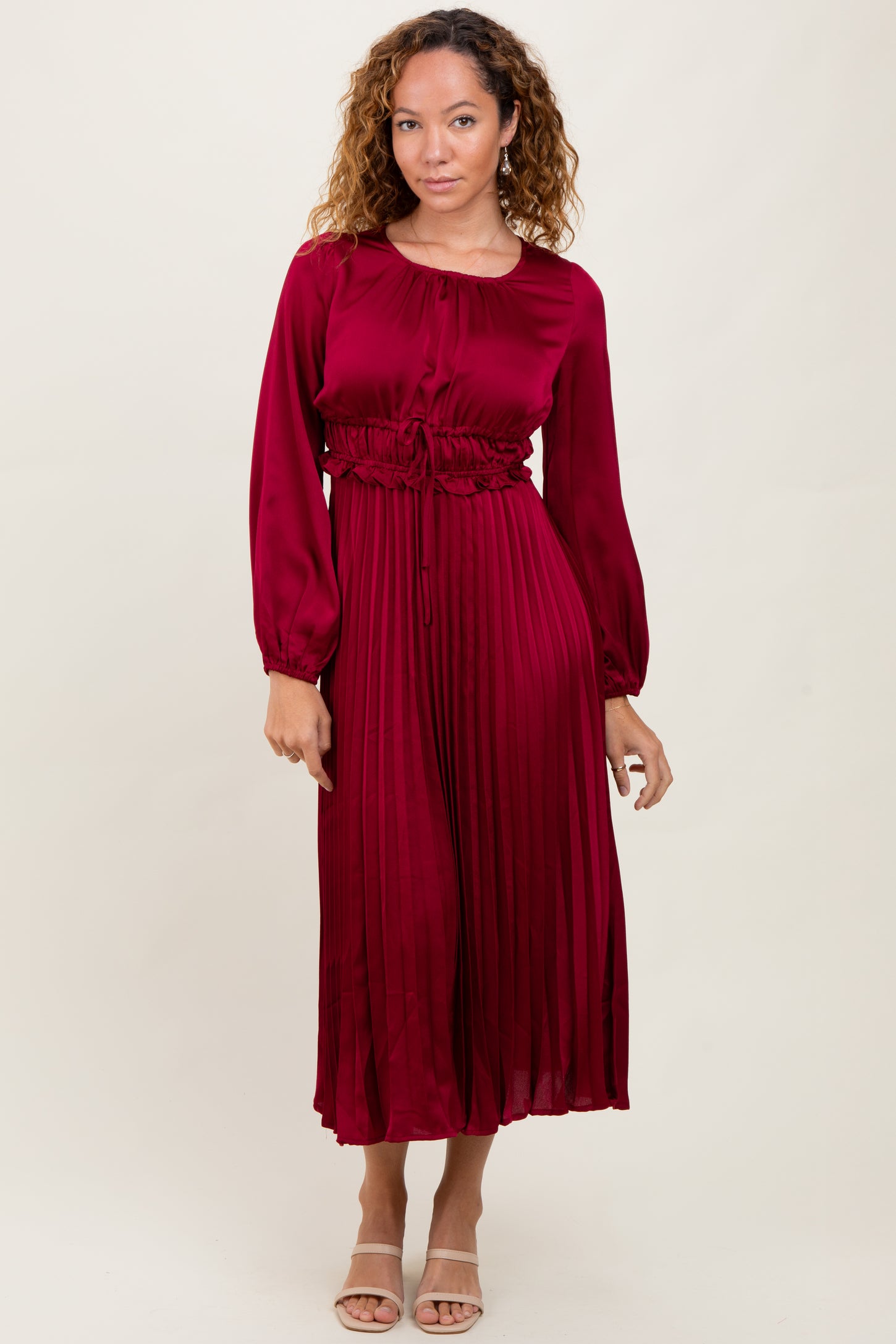 woman wearing a burgundy long sleeve pleated dress with a cinched waist and flowing silhouette