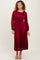 woman wearing a burgundy long sleeve pleated dress with a cinched waist and flowing silhouette