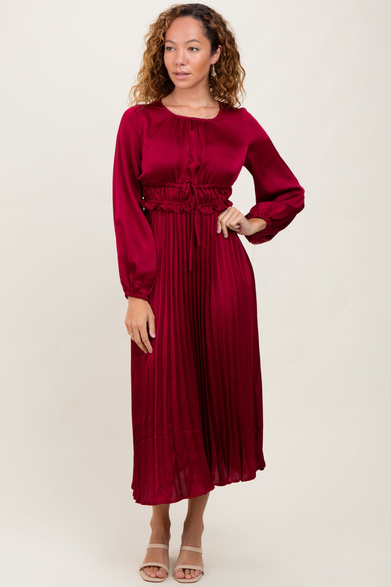 woman wearing a burgundy long sleeve pleated dress with a cinched waist and a rounded neckline
