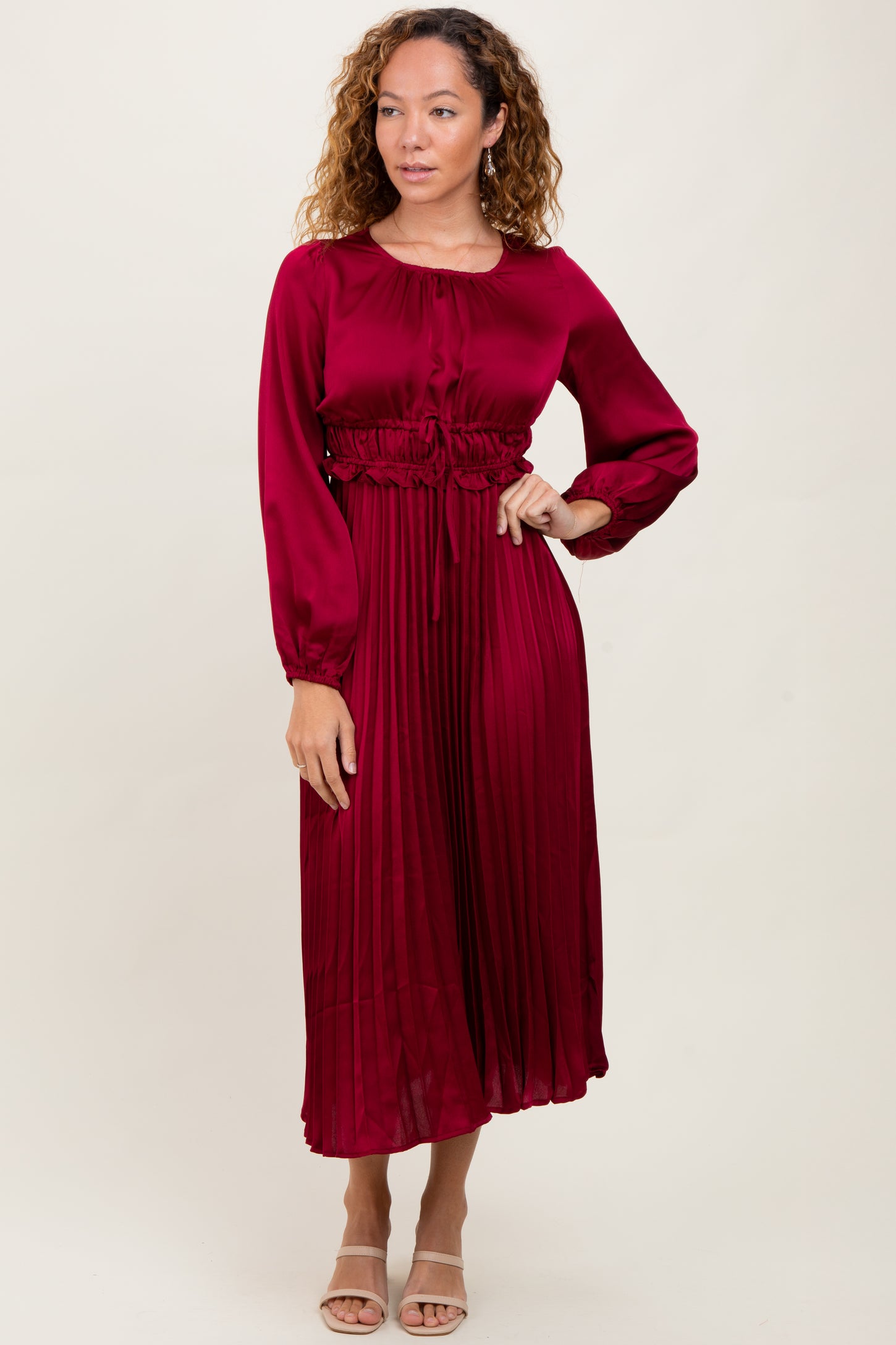 woman wearing a burgundy long sleeve pleated dress with a cinched waist and a rounded neckline