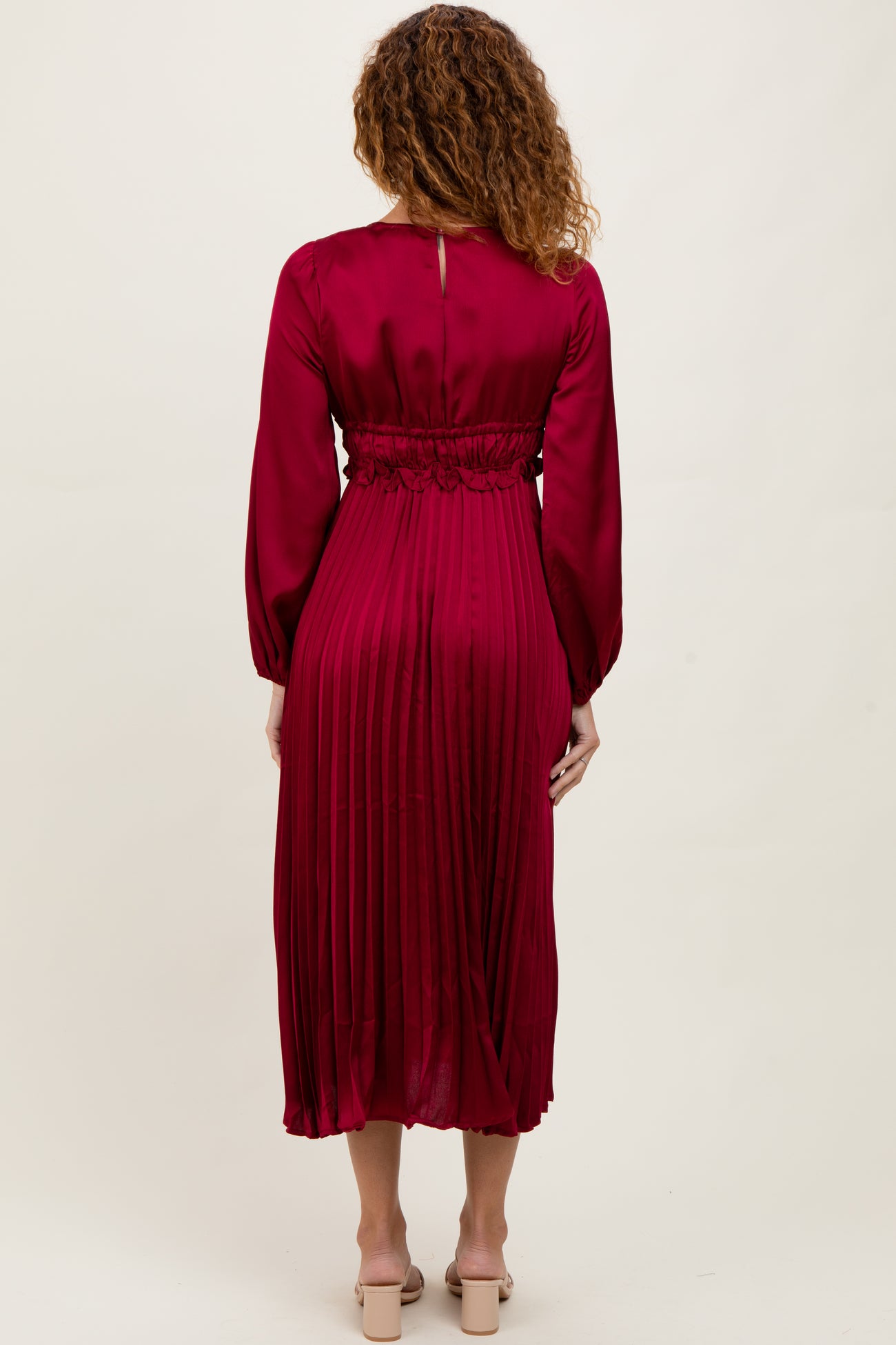 woman wearing a burgundy midi dress with pleated detailing and long sleeves, standing with her back to the camera