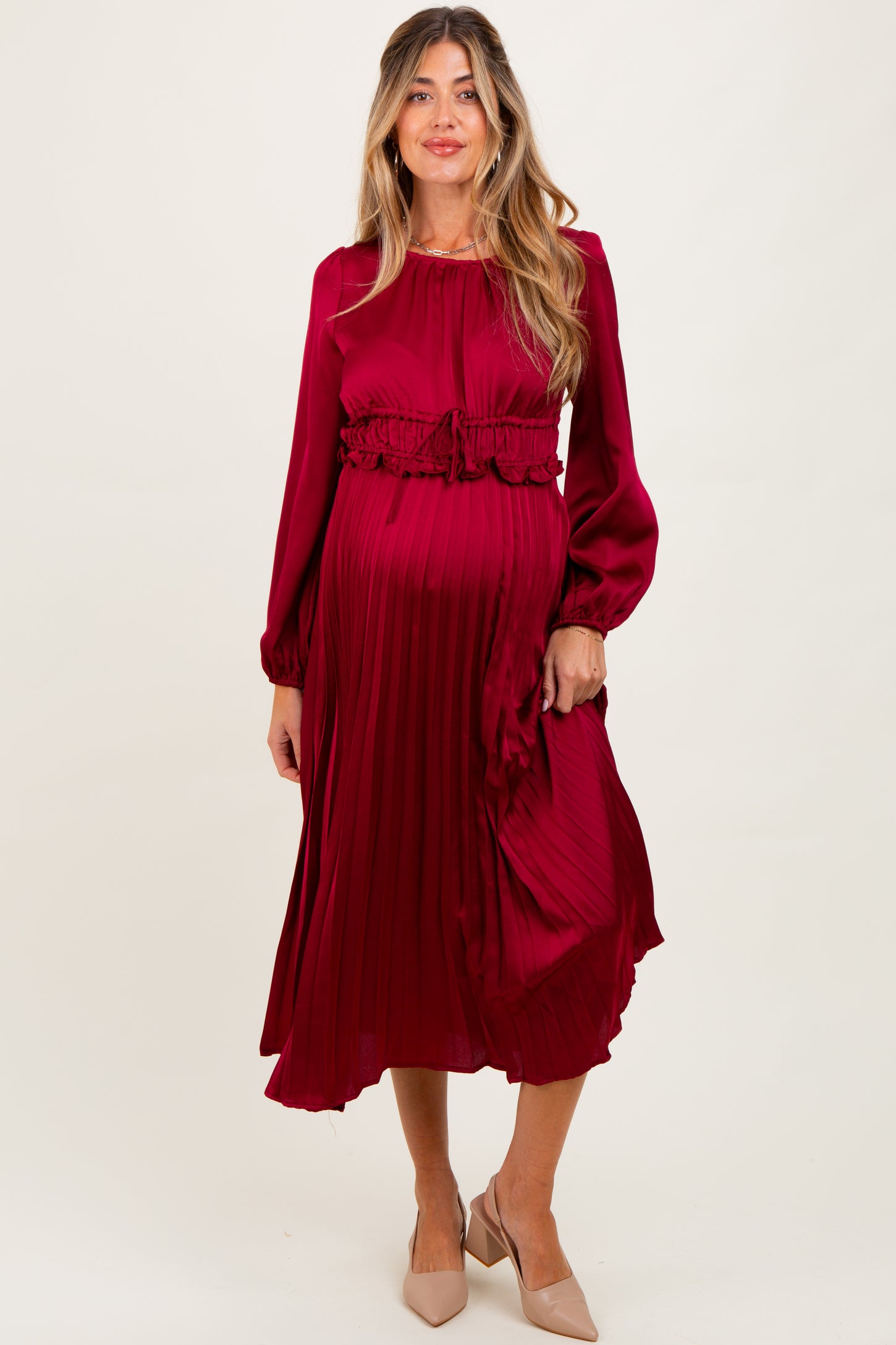 woman wearing a burgundy maternity pleated dress with ruffle details and a visible baby bump