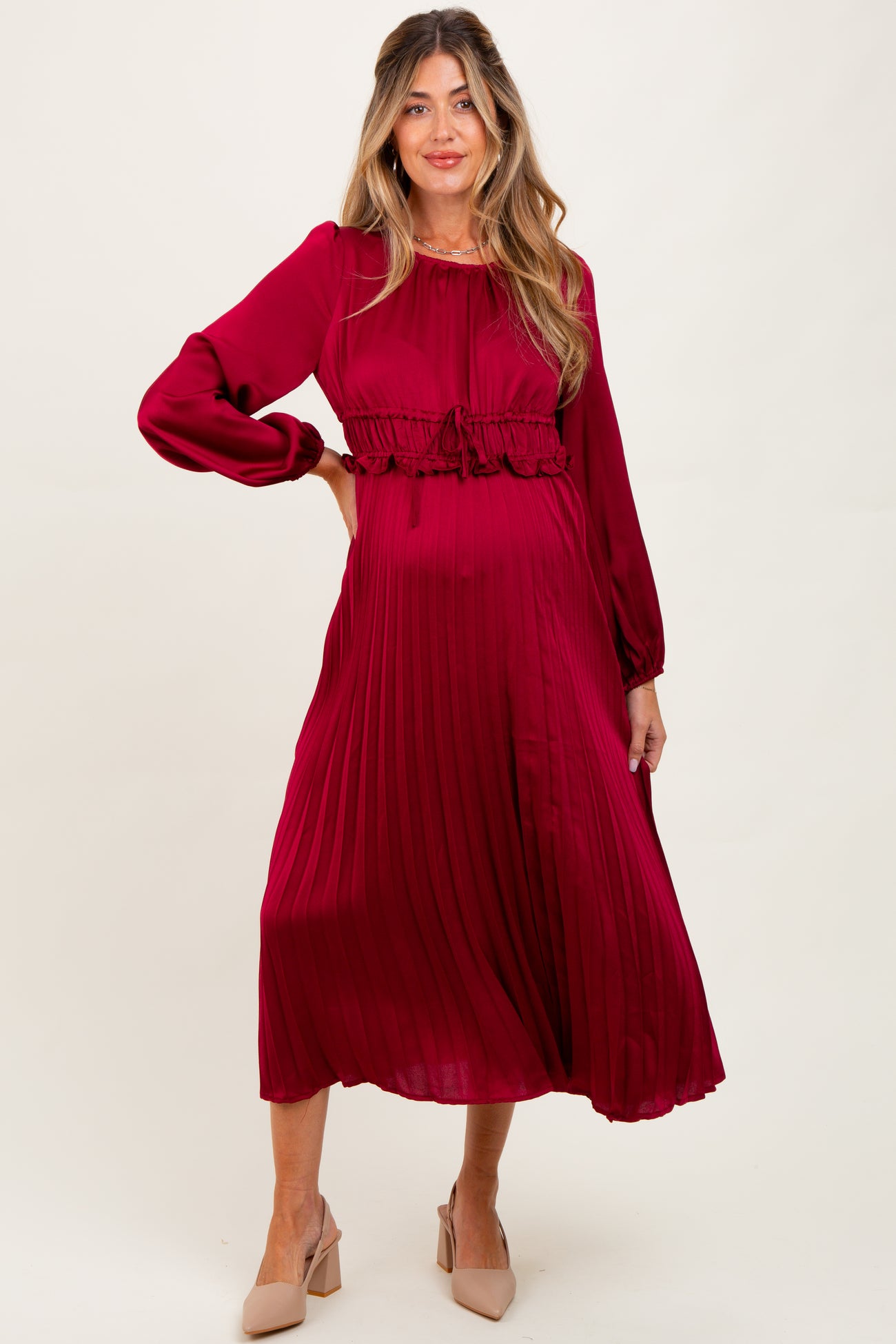woman wearing a burgundy pleated maternity dress with ruffled details and long sleeves, showcasing her baby bump