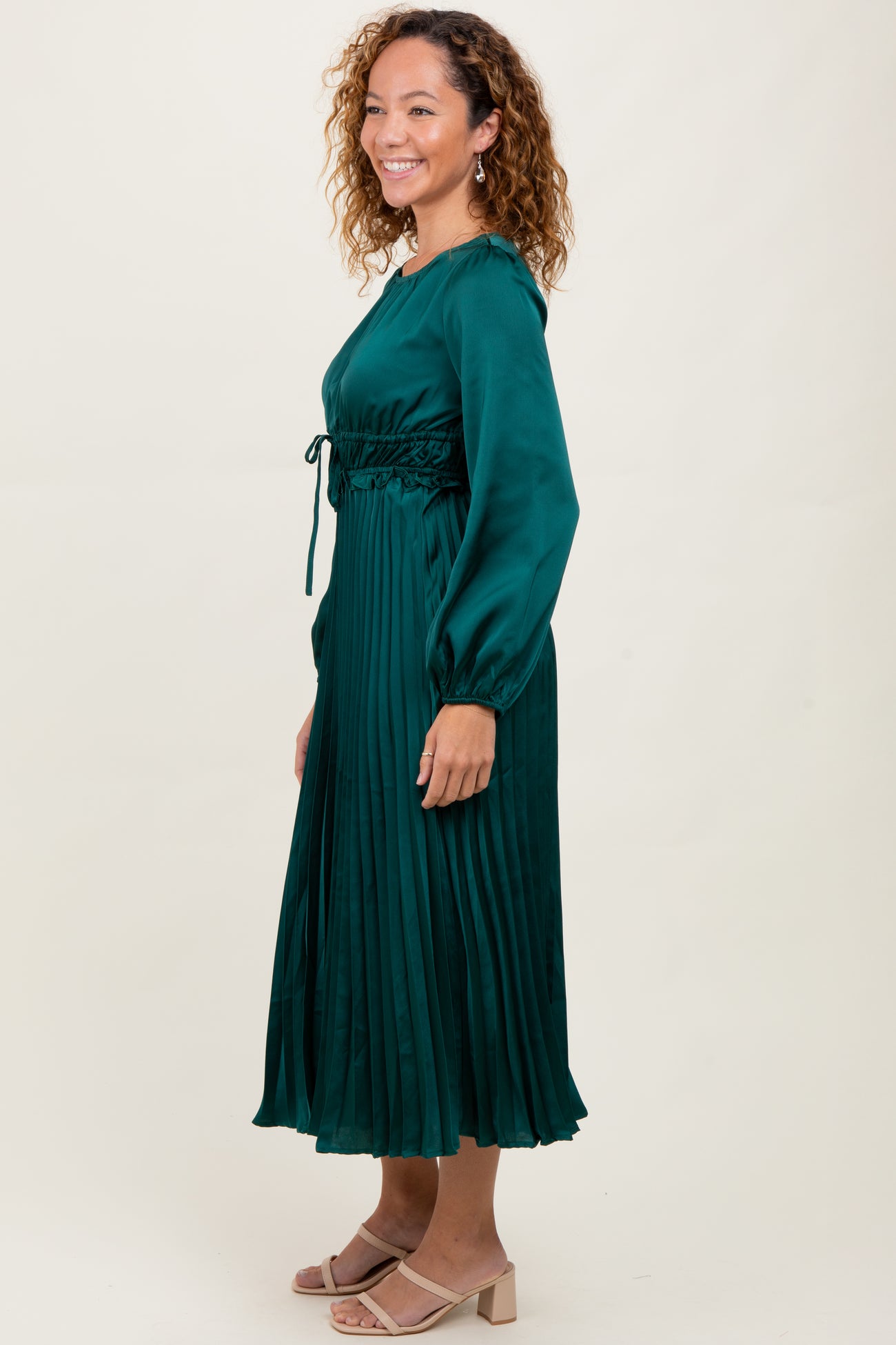 woman wearing a dark green pleated long sleeve dress with a drawstring waist and soft sheen finish