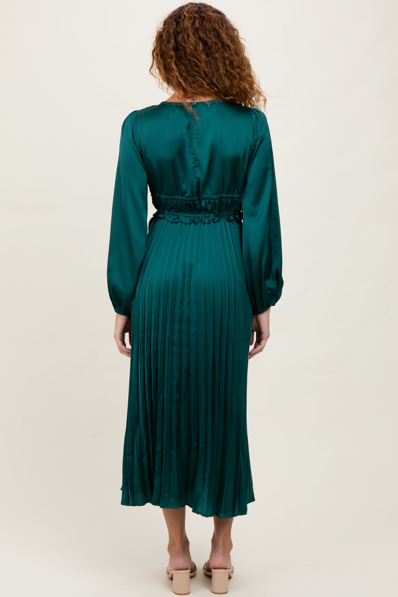 woman wearing a long sleeve emerald green pleated dress with a cinched waist, viewed from the back