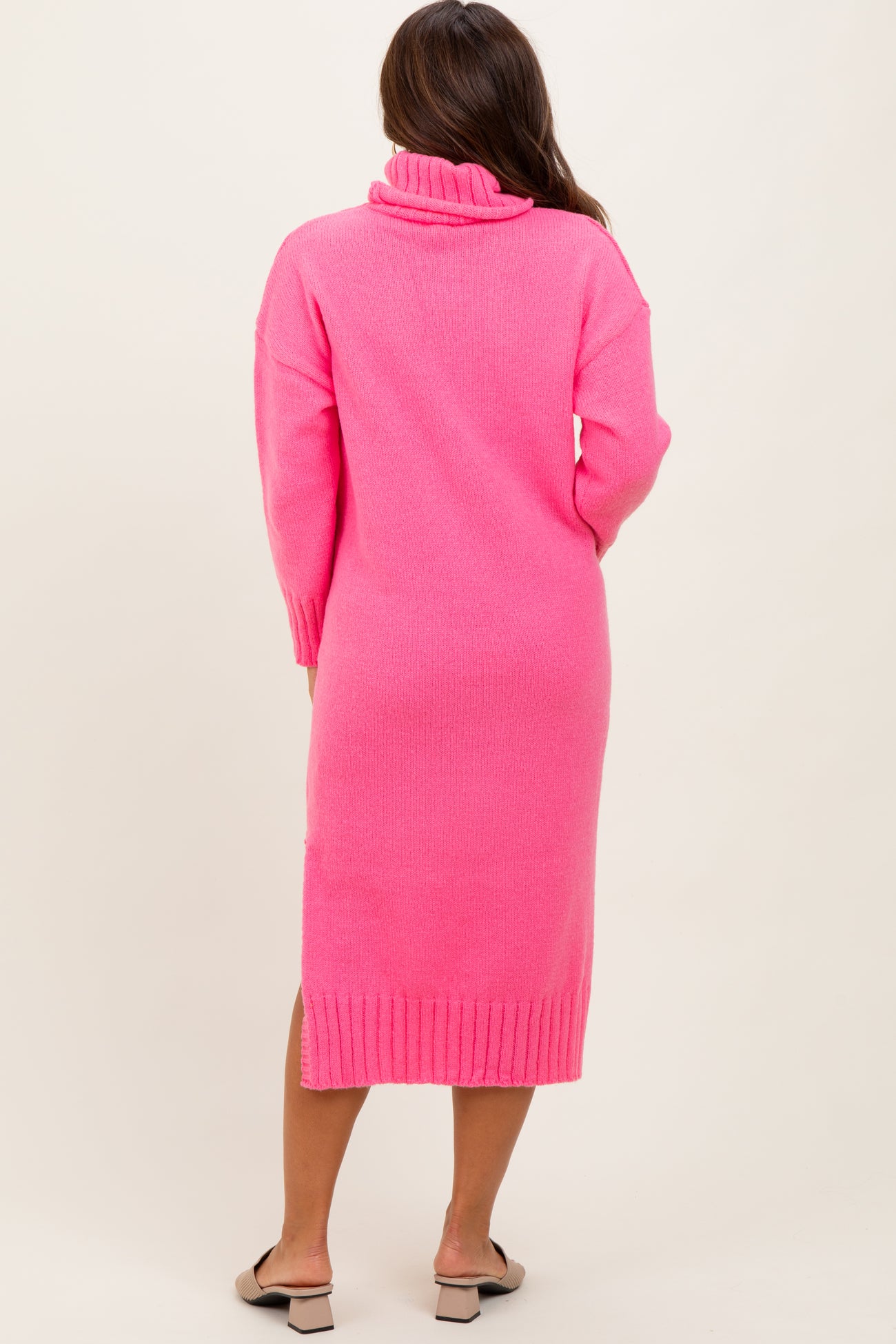 woman wearing a pink long sleeve maternity sweater dress with a turtleneck and a ribbed hem