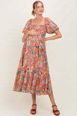 woman wearing a floral print maternity dress with square neckline, puff sleeves, and tied waist, holding her baby bump