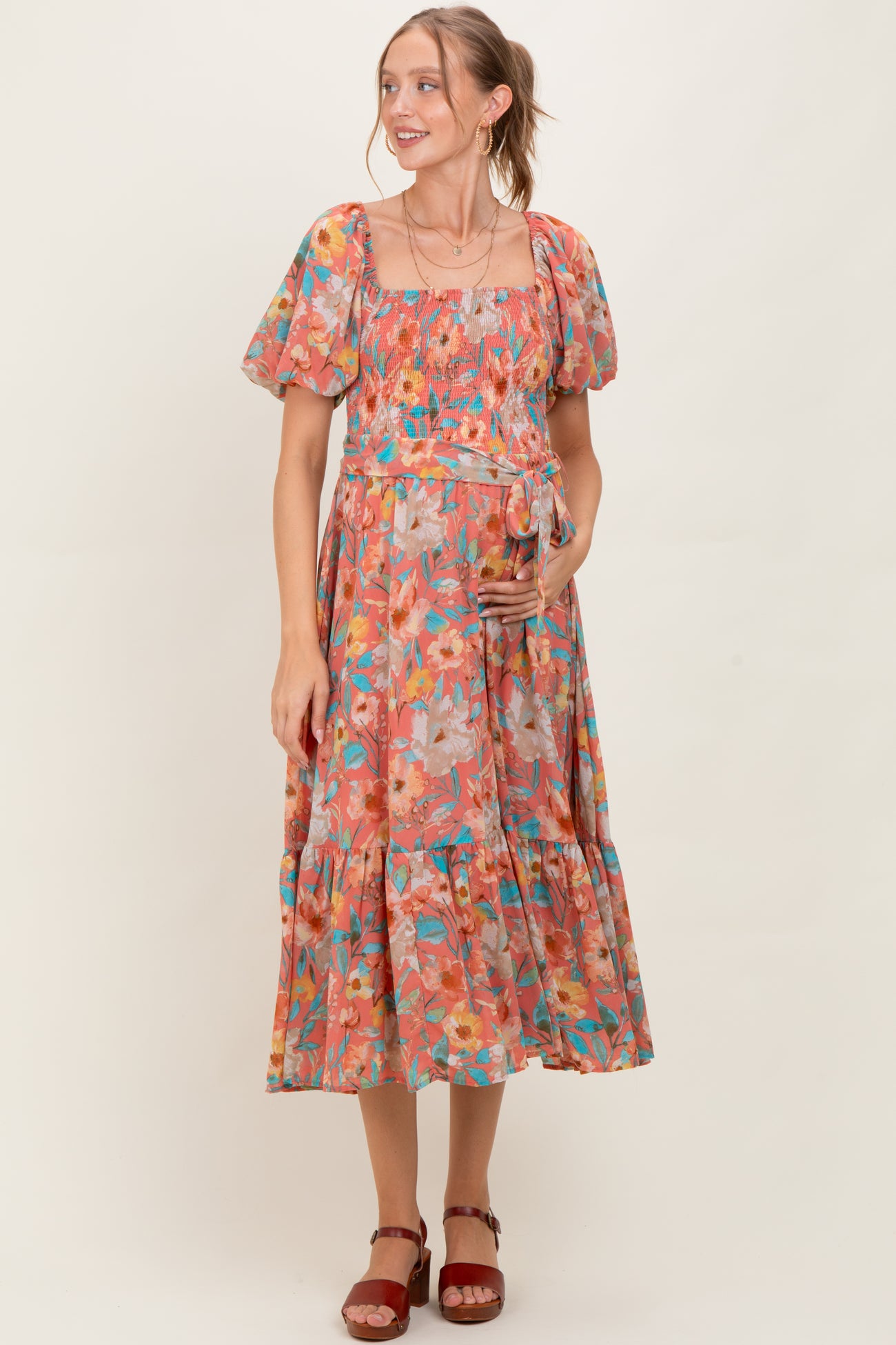 woman wearing a floral print maternity dress with puff sleeves and a tiered skirt, holding her baby bump