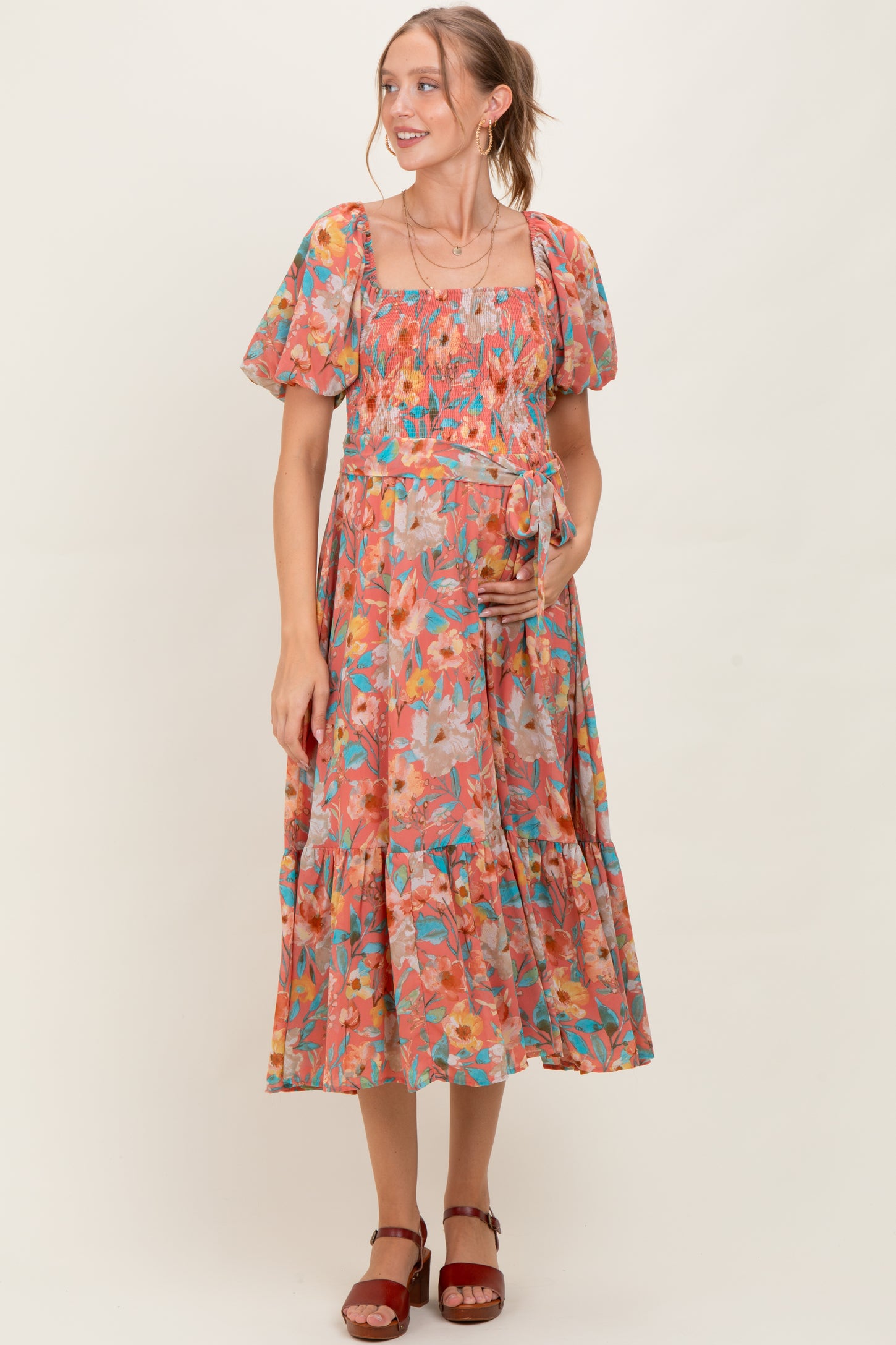 woman wearing a floral print maternity dress with puff sleeves and a tiered skirt, holding her baby bump