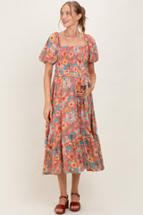 woman wearing a floral print maternity dress with puff sleeves and a tiered skirt, holding her baby bump