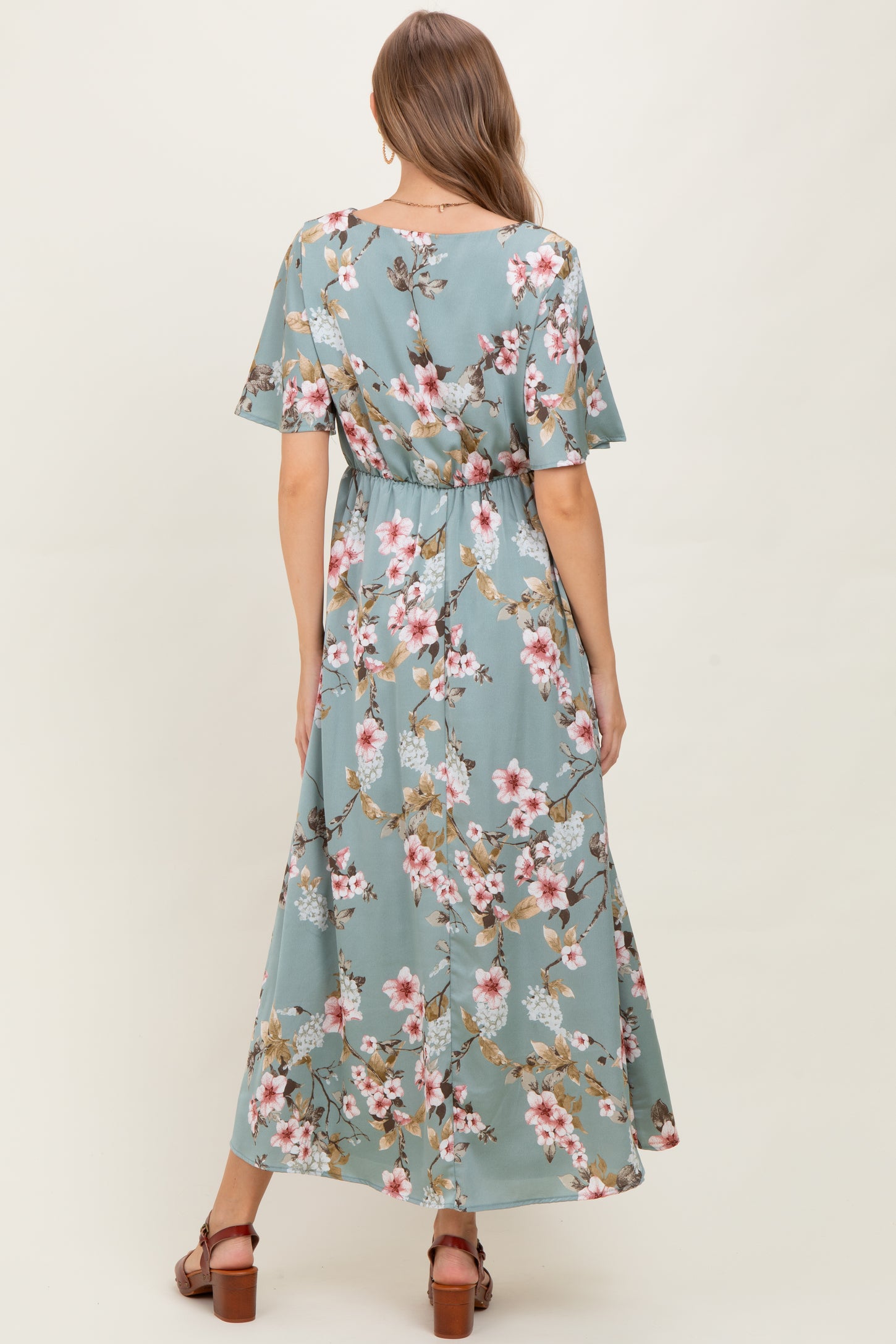 woman wearing a floral patterned maternity maxi dress in light blue with short sleeves and a cinched waist, showing a baby bump
