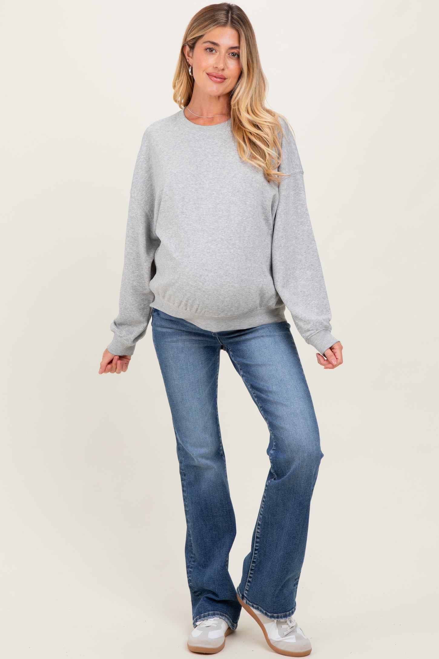 woman wearing a gray long sleeve maternity sweatshirt with a baby bump and light blue flared jeans