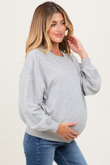 woman wearing a gray maternity sweatshirt and showcasing her baby bump while smiling