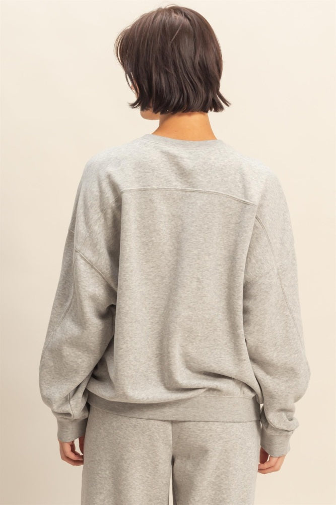 woman wearing a light gray oversized sweatshirt with long sleeves and a relaxed fit, viewed from the back