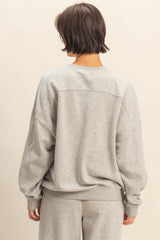 woman wearing a light gray oversized sweatshirt with long sleeves and a relaxed fit, viewed from the back