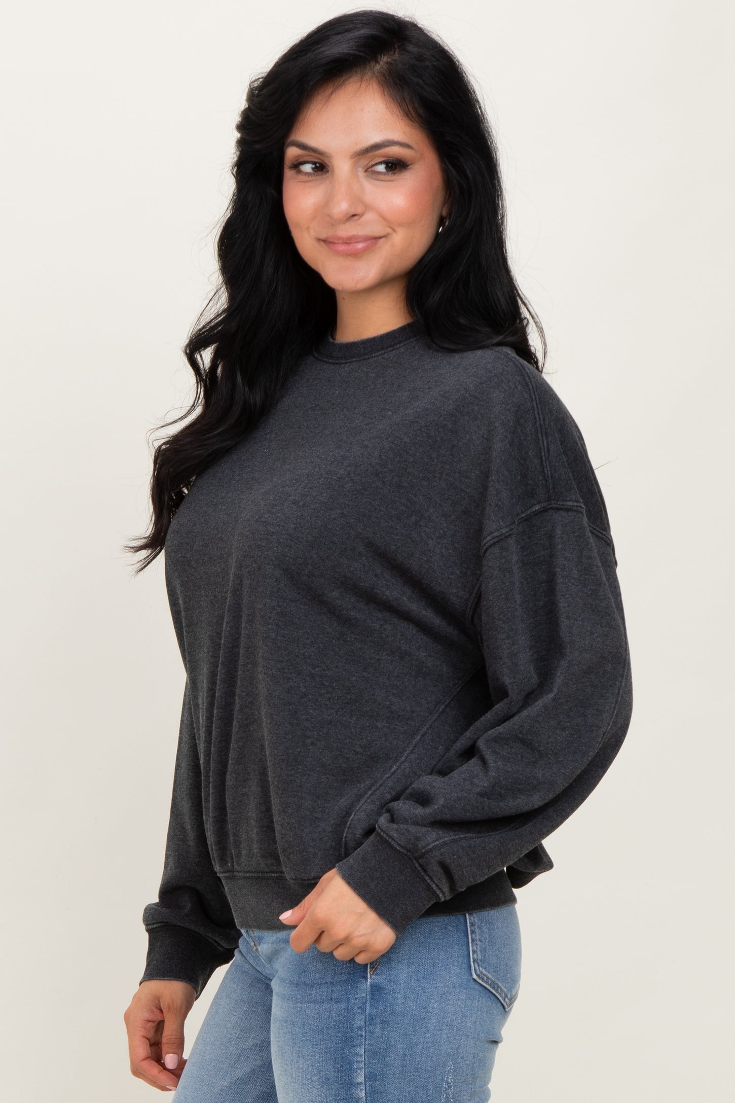 woman wearing a dark gray cropped sweatshirt with a relaxed fit and long sleeves, standing and smiling