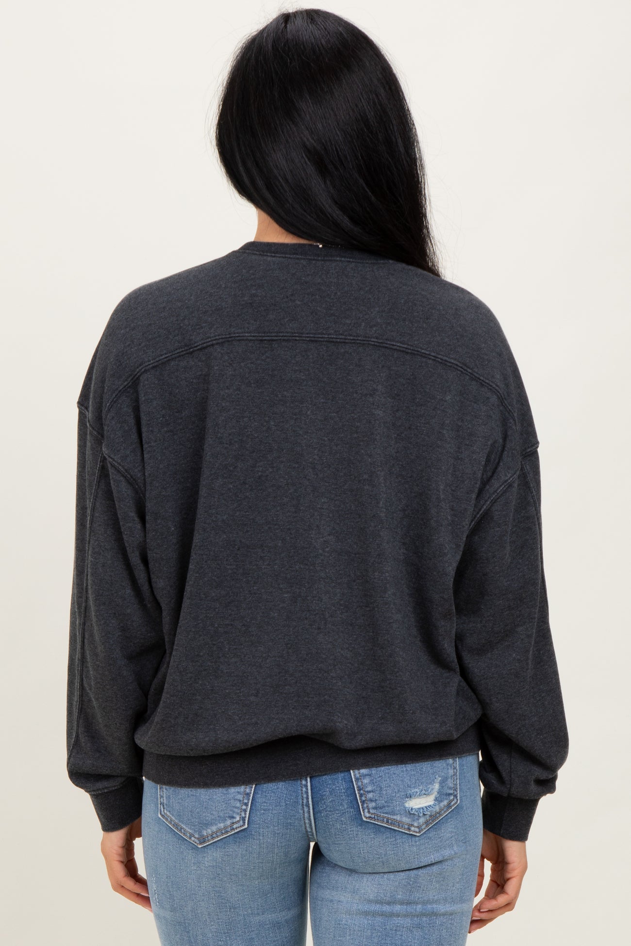 woman wearing a dark grey oversized sweatshirt with dropped shoulders and a relaxed fit paired with light blue jeans