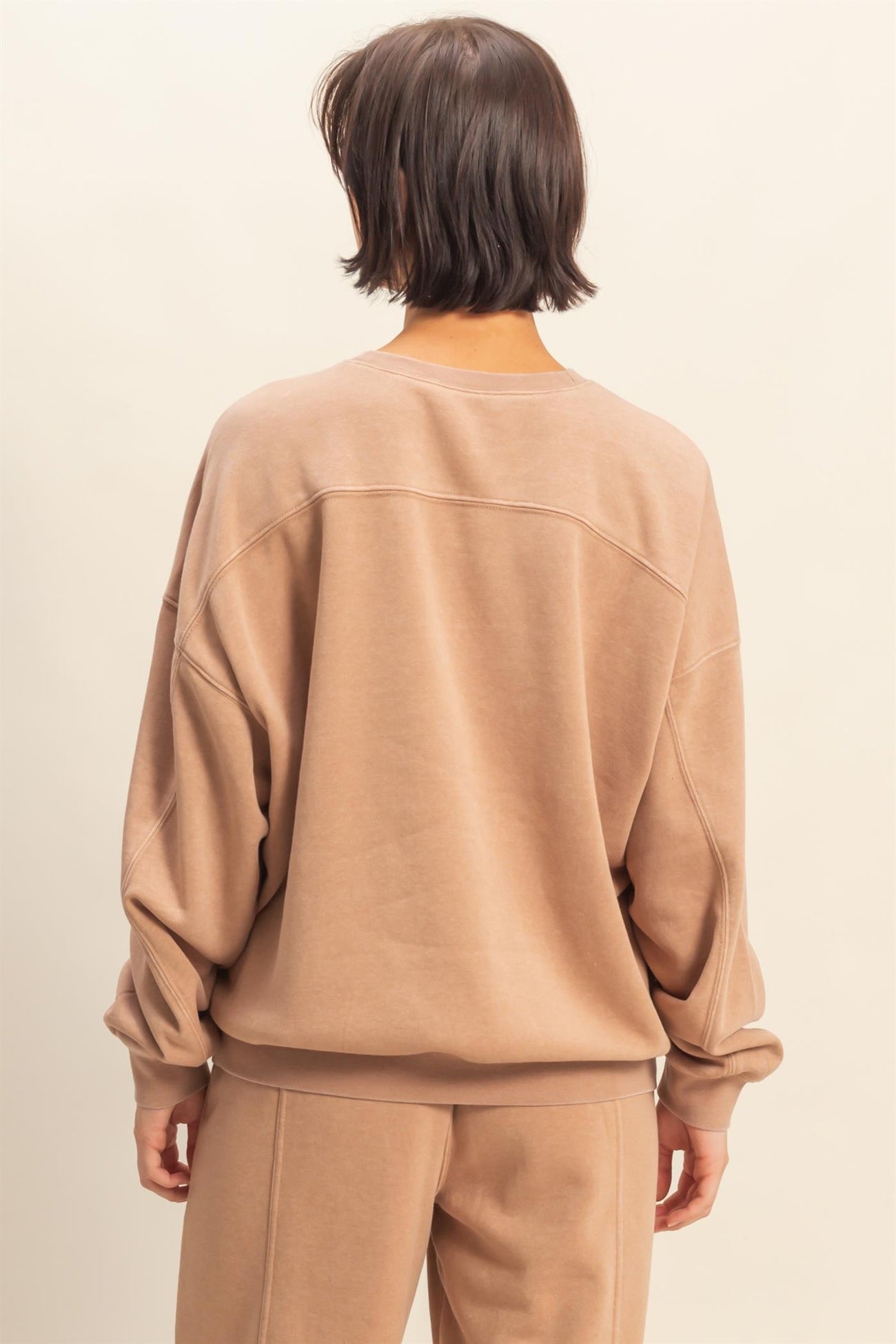 woman wearing a taupe oversized sweatshirt with dropped shoulders and long sleeves, viewed from the back